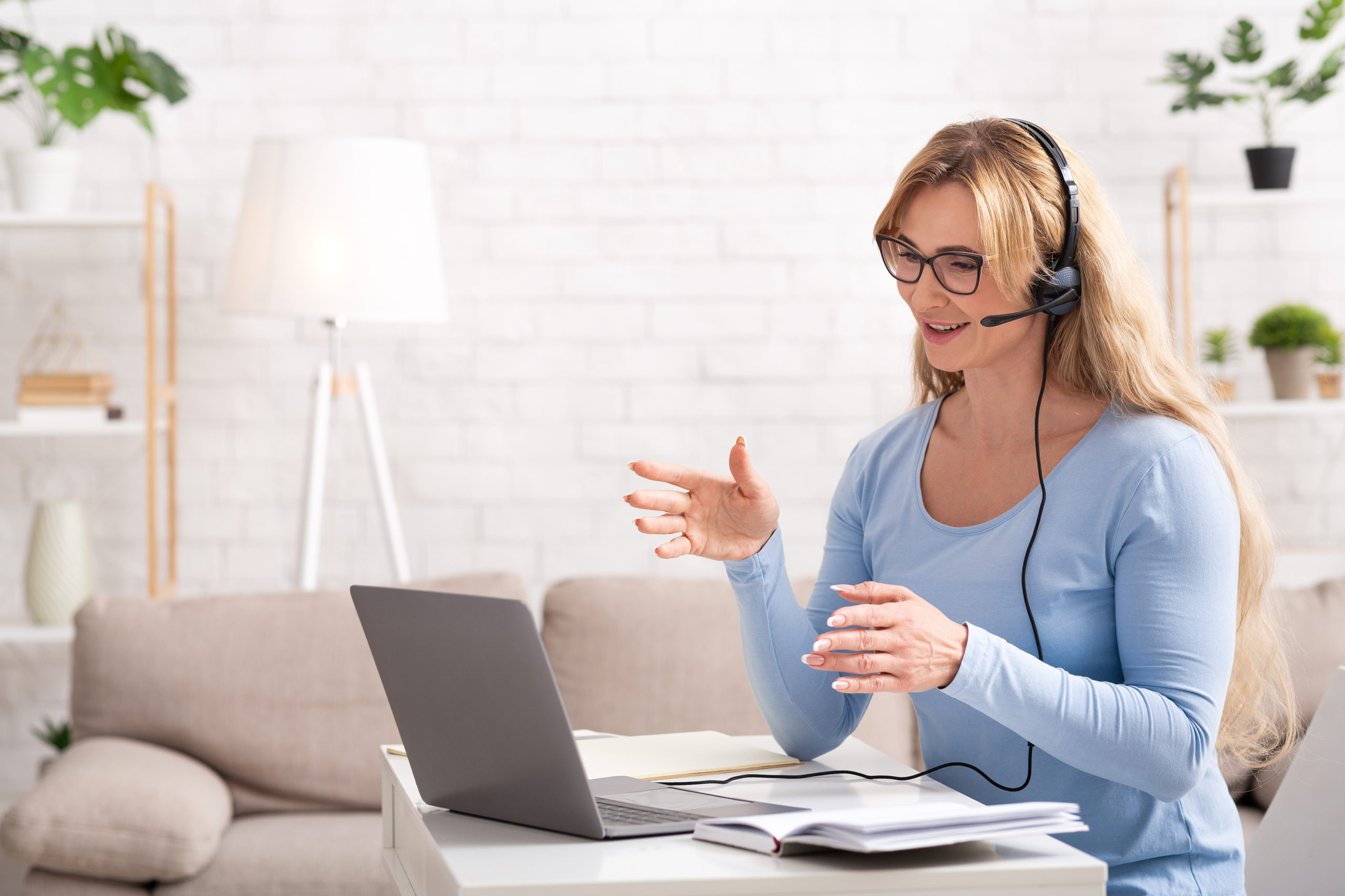 Business video call. Busy woman in glasses and headphones explains to client on laptop, in living room interior